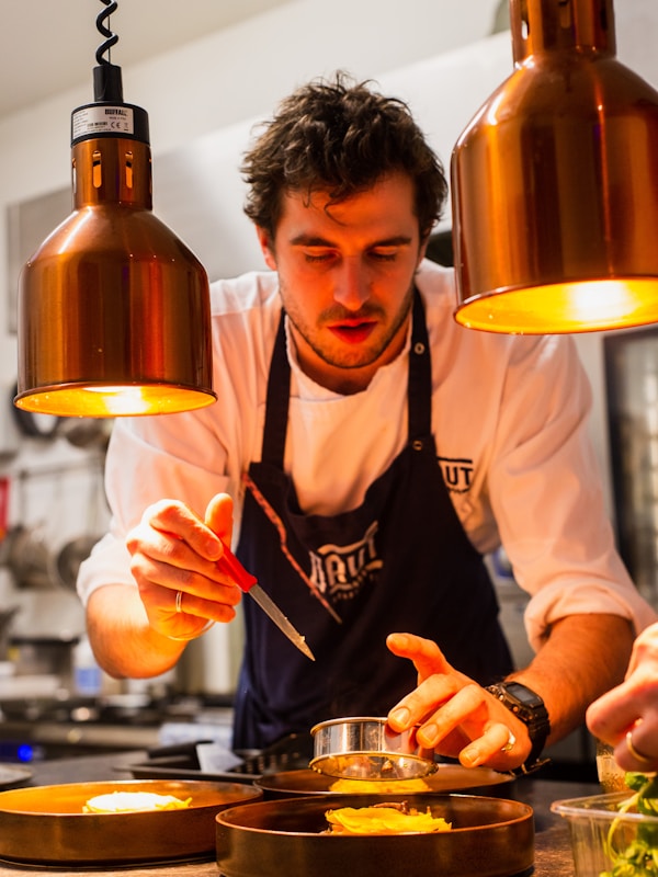 Chef preparing food in professional kitchen wearing custom chef coat and apron by WearUnify